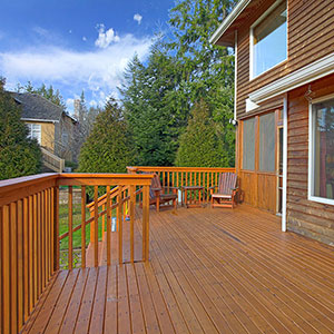 Side view of a home with a large brown deck that has two seats and a small table towards the end