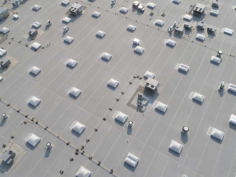 Top view of a white, flat commercial roof with skylights and AC units