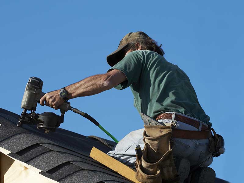 Close up of a worker installing new shingles on a residential roof with a nail gun
