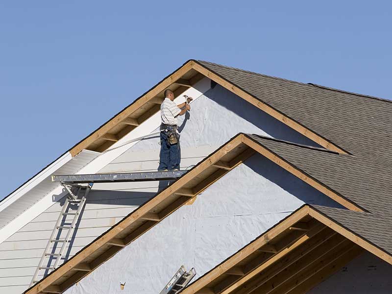 Worker on a platform installing brand new light gray vinyl siding on a home